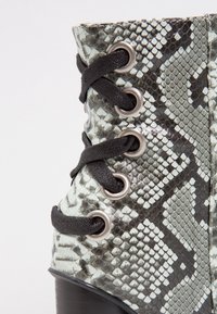 Bottes montantes avec un imprimé serpent noir et blanc texturé, dotées de lacets noirs et d'œillets métalliques, d'une pointe arrondie et d'un talon robuste.