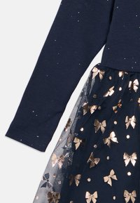 Vestido de manga longa azul-marinho com saia de tule, apresentando um laço brilhante em rosa-dourado e padrões de bolinhas.