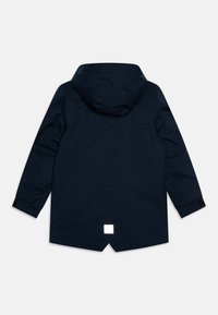 Giacca impermeabile blu marina con cappuccio, maniche lunghe e un dettaglio quadrato riflettente sul retro. Presenta una vestibilità dritta e una texture liscia.