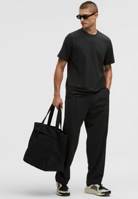 Svart t-shirt och byxor, båda löst sittande. Svart toteväska med överdel och sidodragkedja. Skorna har en blandning av svart med krämfärgade accenter.