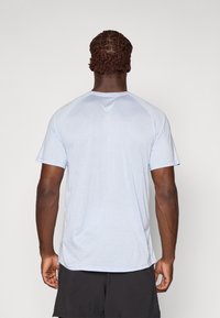 Tricou sportiv cu mânecă scurtă, de culoare albastru deschis, fabricat dintr-un material neted și ușor. Prezintă mâneci raglan și o ușoară curbă la tiv.