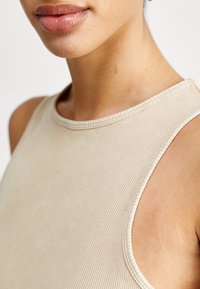 Beige ribbad linne med rund halsringning och ärmlös design, med subtila sömdetaljer och en mjuk textur.