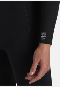 Czarny piankowy kombinezon o grubości 3/2 mm, z gładką teksturą, szwem szwalnym i logo Foil Series w pobliżu nadgarstka.