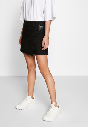 Sort tekstureret mini nederdel med en sidelukning, parret med hvide sneakers. Nederdelen har et klart, lige snit.