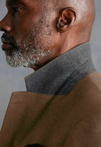 Brown wool coat with a high gray felt collar. The fabric has a smooth texture, highlighting the collar's distinct layered design.