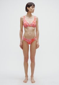 Floral printed bikini set in coral shades. The bralette features underwire support and wide straps; the bottoms are low-rise with side coverage.