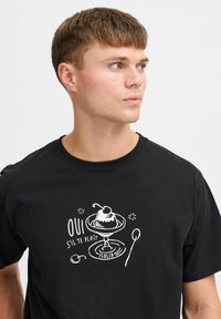 Camiseta negra de algodón, con un estampado gráfico en blanco que representa un postre y el texto "Oui s'il te plaît" en una fuente divertida.