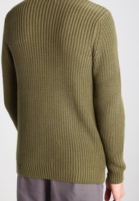 Maglione lavorato a maglia verde oliva con texture a costine. Presenta maniche lunghe e collo tondo. Design semplice senza loghi o decorazioni visibili.