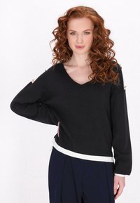 Black knit sweater with a V-neck, long sleeves, and white hem accents. Notable details include shoulder hardware and a relaxed fit.