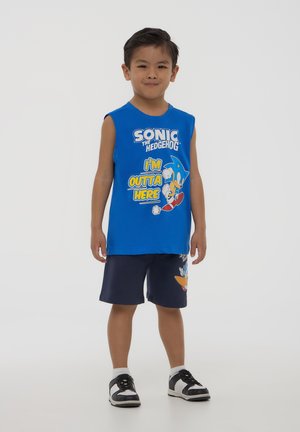 Maglietta senza maniche blu con grafica di "Sonic the Hedgehog", abbinata a pantaloni corti blu marina con stampa di personaggi. Sneakers bianche e nere.