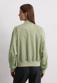 Light green bomber jacket with a ribbed collar and cuffs, featuring a smooth, shiny texture and drop shoulders. Back view displayed.