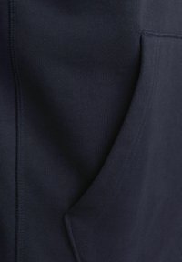 Sweat à capuche bleu marine avec une texture lisse, présentant une poche avant et des détails sur les coutures latérales. Fabriqué à partir d'un tissu doux et extensible.