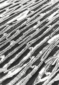 Tessuto nero con paillettes silver metallizzate disposte in linee ondulate, creando una superficie testurizzata e riflettente.