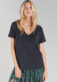 T-shirt noir à col en V avec des manches courtes. Tissu doux, coupe décontractée, texture lisse. Associé à une jupe à motifs verts et bleus.