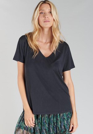 T-shirt noir à col en V avec des manches courtes. Tissu doux, coupe décontractée, texture lisse. Associé à une jupe à motifs verts et bleus.