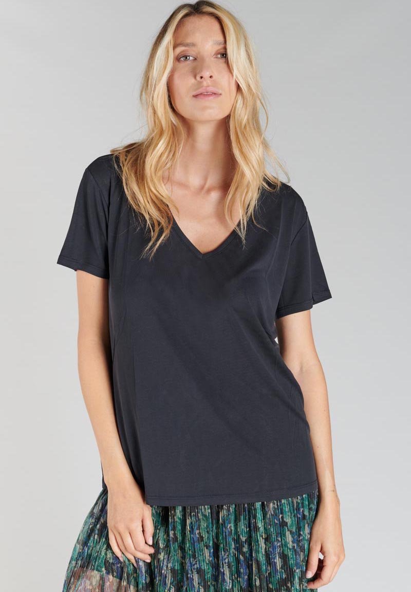 T-shirt noir à col en V avec des manches courtes. Tissu doux, coupe décontractée, texture lisse. Associé à une jupe à motifs verts et bleus.