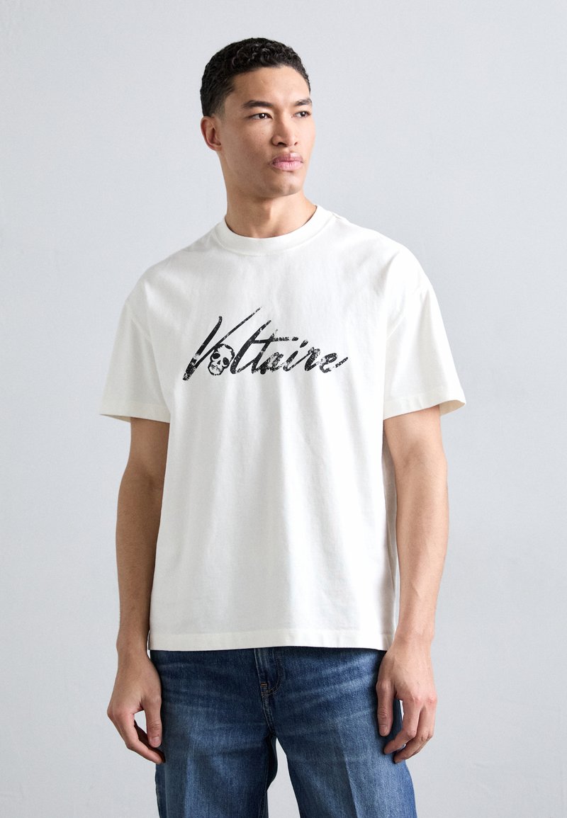 Camiseta de algodón blanca con "Voltaire" impreso en una fuente gráfica negra y en negrita. Mangas cortas, cuello redondo clásico, corte relajado.