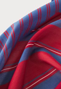 Rot-blau gemusterter Schal, mit auffälligen Streifen und leichtem Textil, sowie subtilen weißen Akzenten. Das Material wirkt weich und leicht.