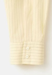 Rokav kremne barve s tankimi navpičnimi in vodoravnimi črtami, s manšetom z dvema belima gumboma.