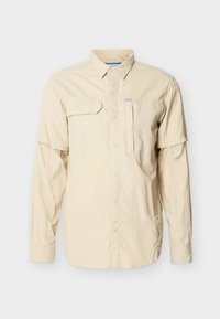 Μπεζ πουκάμισο με μακριά μανίκια και αποσπώμενα μανίκια με φερμουάρ, κλείσιμο με κουμπιά, θηλυκή τσέπη στο στήθος με καπάκι και γιακά.