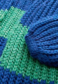 Gebreide deken met een mix van donkerblauwe en groene garens, met textuurpatronen en een zachte, pluizige afwerking.