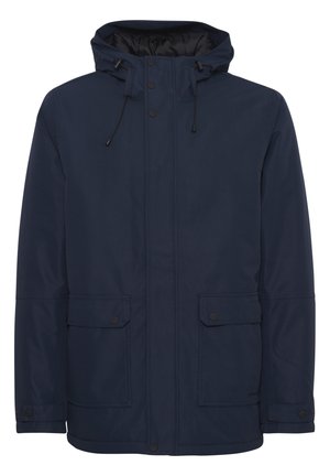 Chaqueta impermeable en azul marino con capucha, que cuenta con cierres frontales a presión, cordón ajustable y dos bolsillos frontales tipo parche. Textura suave.