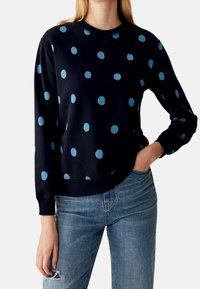 Sudadera de la marina con lunares azul claro, cuello redondo, mangas largas y puños acanalados. Combinada con jeans desgastados de color azul claro.