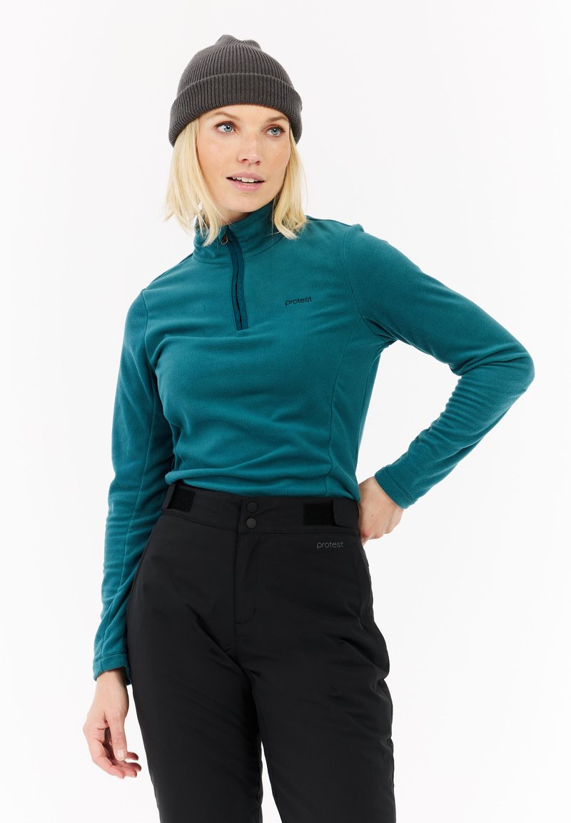 Pull en polaire bleu canard à zip quart avec un col montant et un logo sur la poitrine gauche, associé à un pantalon noir avec deux boutons et des accents en velcro.