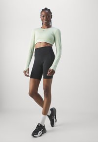 Világoszöld hosszú ujjú crop top, fekete magas derekú sort, fekete sportcipő fehér részletekkel, és fehér bokazokni. Simára kidolgozott anyagok.