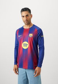 Dugulje sa dugim rukavima FC Barcelone koja sadrži plave i crvene pruge, Nike logo, Spotify krug na prednjoj strani i detalj oznake sa strane.