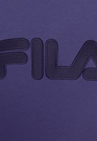 Mörkblå upphöjd brodyr som staver "FILA" på bakgrund av lila stickad tyg.