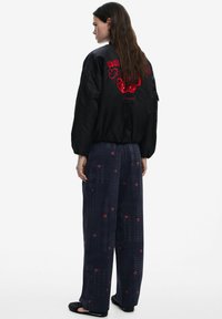 Čierna bomber bunda s červeným grafickým dizajnom, skombinovaná s modrými voľnými nohavicami s malými červenými vzormi čerešní.