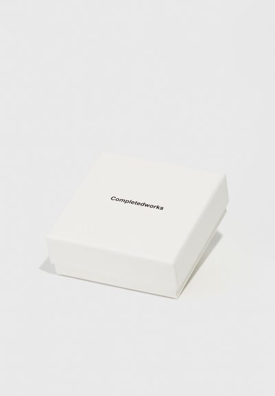 White square box made of textured paper, featuring the brand name "Completedworks" printed in black on the top. Minimal design.