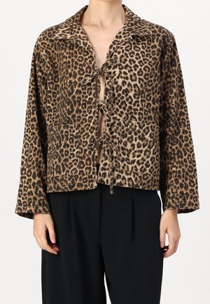 Leoprint-Longsleeve-Jacke mit weitem Kragen, vorderen Binderverschlüssen und aufgesetzten Fronttaschen, getragen zu schwarzen Hosen.