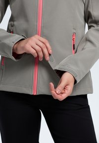 Gray softshell jacket with pink zippered accents. Features a close-up of the cuff and hand adjusting the sleeve, highlighting detail and texture.
