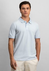 Lys blå polo skjorte laget av bomull med en treknappslukking, korte ermer og en subtil logo brodert på brystet.