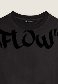 Camiseta de algodón negra con un gráfico grande, audaz y negro que dice "Flow" en el pecho. Cuello redondo con detalle de costura estándar.