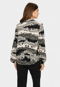 Blouse fluide noir et blanc avec un motif floral, arborant des manches longues et un ourlet arrondi. Le tissu a une texture lisse.