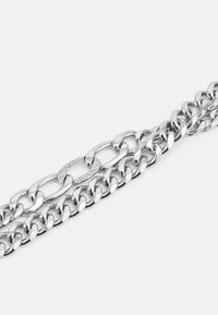 Colar de corrente prateada com elos grossos, apresentando um elo central a brilhar adornado com pequenos cristais, acabamento em metal polido.