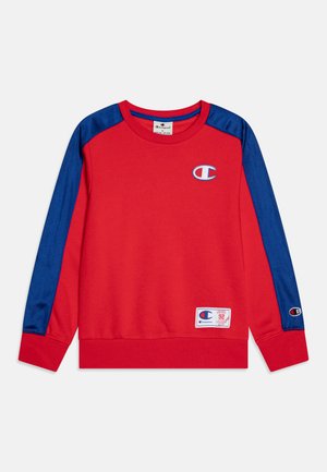 Rode sweatshirt met blauwe satijnen mouwen, ronde halslijn, geribde manchetten en onderrand. Voorzien van een klein logo op de borst en een accentpatch onderaan.