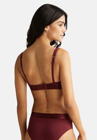 Reggiseno bordeaux con spalline regolabili, tessuto morbido e chiusura a gancio. Presenta un marchio in caratteri scuri sul cinturino.
