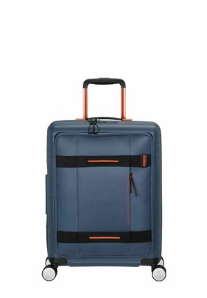 Valise rigide en tissu bleu foncé avec des accents rouges. Dotée d'une poignée rétractable, de quatre roues et de compartiments zippés.