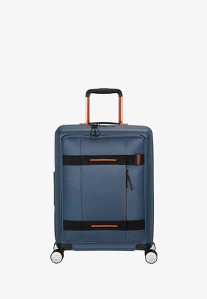 Valise rigide en tissu bleu foncé avec des accents rouges. Dotée d'une poignée rétractable, de quatre roues et de compartiments zippés.