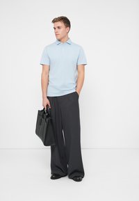 Gaiši zils polo krekls ar apkakli, apvienots ar platiem tumši pelēkiem biksēm. Individuāls nēsā melnu ādas rokassomu.