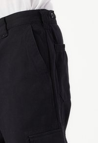 Schwarze Baumwoll-Cargo-Hosen mit Knopfverschluss, Seitentaschen und strukturiertem Finish. Sie verfügen über einen geraden Schnitt und eine elastische Tasche.