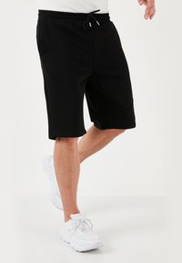Pantaloni sportivi neri realizzati in tessuto morbido, dotati di una cintura elastica con cordoncino, taglio fino al ginocchio e tasche laterali.