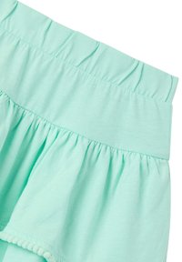 Indumento in cotone verde menta con vita arricciata e orlo a volant, caratterizzato da un bordo in pompon testurizzato lungo il margine inferiore.
