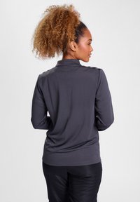Graues Langarmshirt mit strukturiertem Muster, minimalem Kragen und Schulterakzenten. Der Stoff wirkt glatt und leicht.