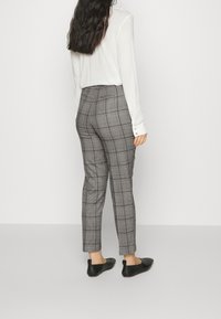 Pantalon ajusté à carreaux gris avec une coupe slim, présentant une texture lisse et un détail subtil de poche, associé à un haut blanc à manches longues.