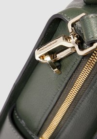 Close-up van een donker groen leren tashoek met een gouden rits en gouden slotbeslag.